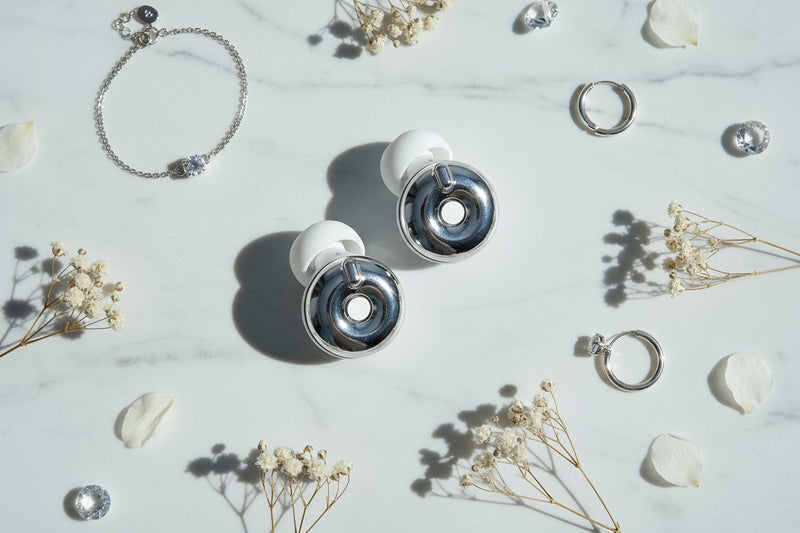 Bouchons d'oreilles QUIET Adapte argentés avec embouts en silicone blanc sur un fond en marbre élégant