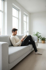 Homme lisant un livre sur un canapé gris portant des bouchons d'oreilles QUIET Adapte pour une concentration optimale