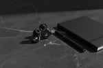 Bouchons d'oreilles QUIET Adapte noirs avec molette ajustable, posés sur une table en marbre près d'un carnet et stylo