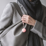 Étui Quiet Sommeil rose accroché à son cordon, tenu à la main contre un sac en cuir gris