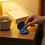 Main qui prend un bouchon d'oreille Quiet Sommeil bleu dans son étui, sur la table de nuit
